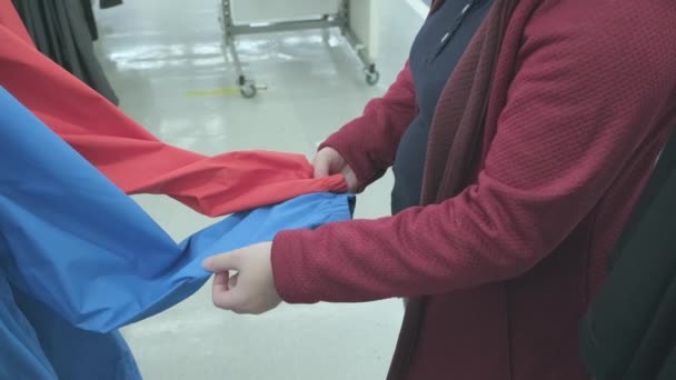 Mujer con vientre redondo elige una chaqueta cortavientos azul y rojo en la tienda para comprar — Vídeo de stock