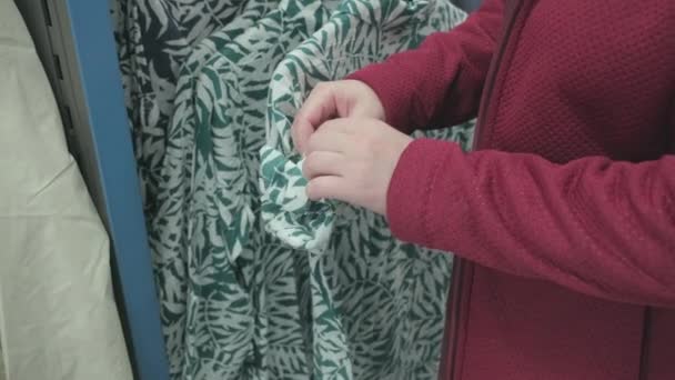 Жінка вибирає зелену сорочку з тропічним візерунком дерева в магазині одягу, щоб купити — стокове відео