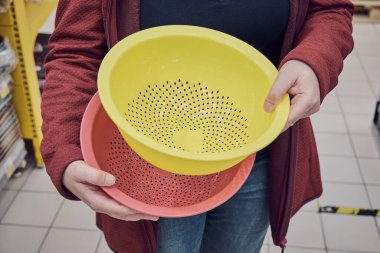 Mağazadaki kız yemek yapmak için büyük plastik bir süzgeç seçiyor.