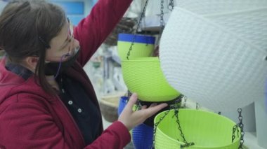 Virüse karşı maskeli bir kadın mağazadaki saksılar için yeşil, plastik saksılar alıyor.