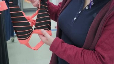 Virüse karşı maskeli bir kadın markette turuncu çizgili mayo seçiyor.