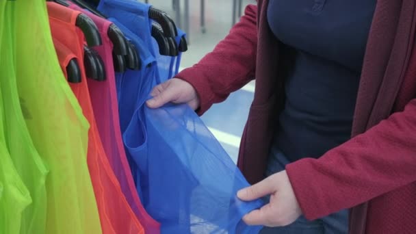 Mujer en la tienda elige una capa reflectante brillante para la ropa. Manos cerca de disparo — Vídeos de Stock