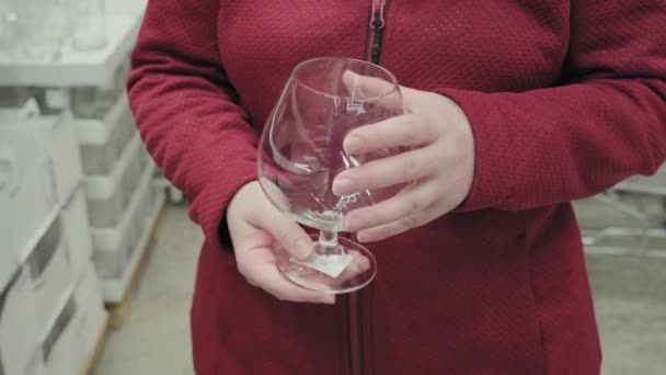 Chica caucásica compra una copa grande y transparente para vino y brandy en una tienda — Vídeos de Stock