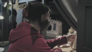 Virüse karşı maskeli bir kadın dikiş atölyesi için iç mekan seçiyor
