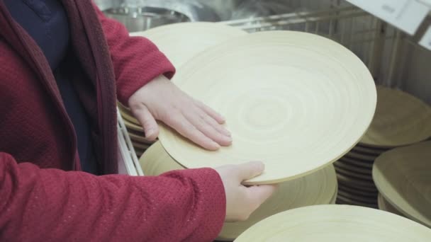 Γυναίκα σε ένα κατάστημα αγοράζει ένα μεγάλο, στρογγυλό ξύλινο πιάτο από φυσικό ξύλο. Κλείσε. — Αρχείο Βίντεο