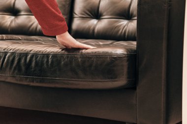 Mağazadaki beyaz kadın kahverengi deriden yapılmış pahalı bir kanepeyi seçiyor.