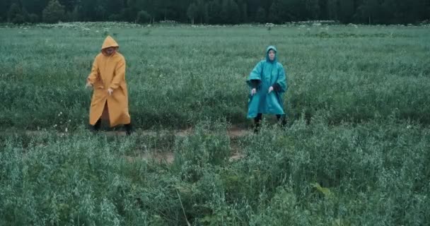 Man in yellow raincoat and a woman in blue raincoat dance in a field — Vídeo de stock