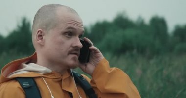 Man is raincoat is talking on phone in nature but connection interrupted