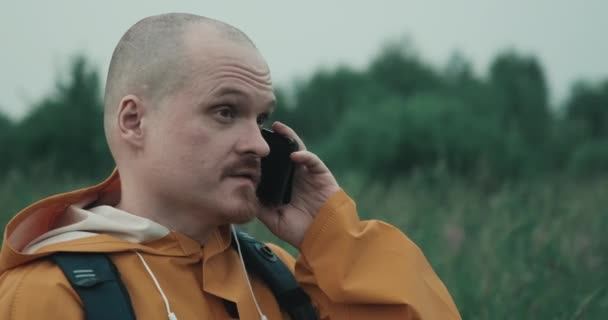 Man is raincoat is talking on phone in nature but connection interrupted — Video