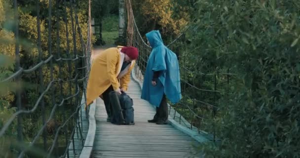 Man and woman hikers, walking on bridge over river, drinking from vacuum flask — Vídeo de Stock