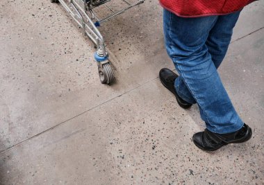 Kadın ayağı alışveriş merkezinde yürür. Bir kadın önünde bir market arabası taşıyor.
