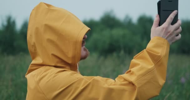 Ο άνθρωπος με το κίτρινο αδιάβροχο με κουκούλα προσπαθεί να πιάσει GPS ή Internet στη φύση — Αρχείο Βίντεο