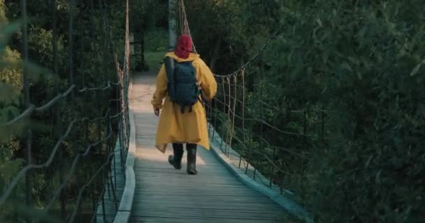 Muž v žlutém plášti kráčí po visutém mostě. Zezadu — Stock video