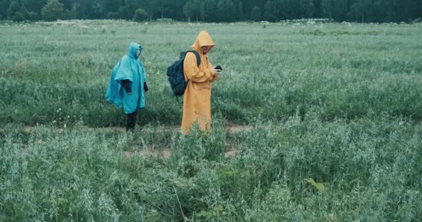 穿着雨衣的男男女女正在穿过田野，用电话看地图 — 图库视频影像