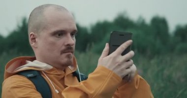 Sarı yağmurluklu adam doğada GPS ya da internet yakalamaya çalışıyor.