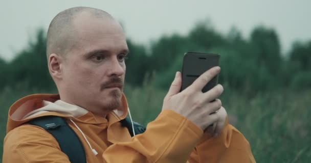 Hombre en impermeable amarillo está tratando de coger GPS o Internet en la naturaleza — Vídeo de stock