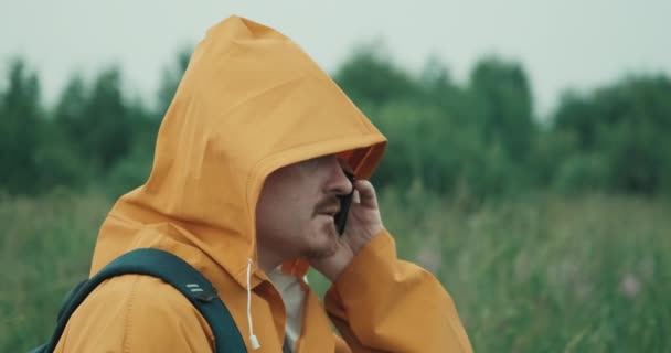 Человек в плаще с капюшоном разговаривает по телефону в природе, связь прервана — стоковое видео
