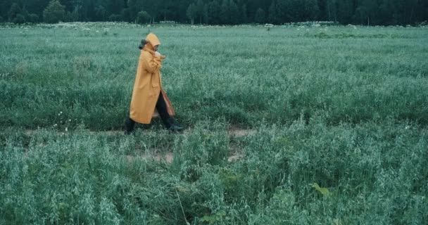 Ο άντρας με το κίτρινο αδιάβροχο και το τσεκούρι περπατά στο χωράφι το σούρουπο. — Αρχείο Βίντεο