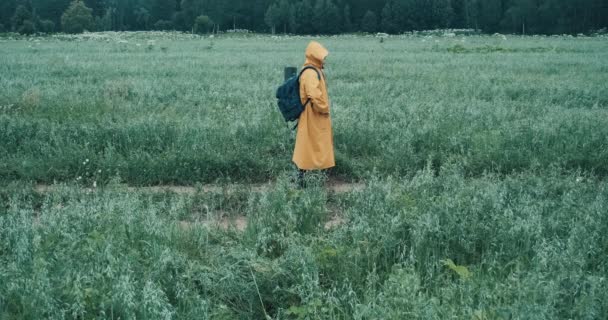 Man in een gele regenjas loopt door een veld en kijkt naar een kaart in zijn telefoon — Stockvideo