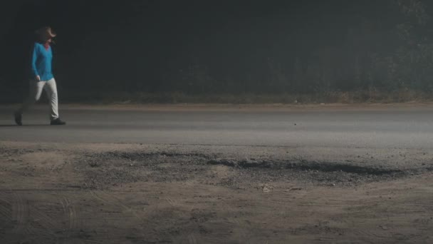 Człowiek w kowbojskim kapeluszu i źdźbło trawy w ustach spaceruje po nocnej drodze — Wideo stockowe