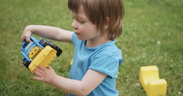 Copilul drăguț se joacă cu mașina de jucărie și cuburi pe iarbă verde. Portret aproape — Fotografie, imagine de stoc