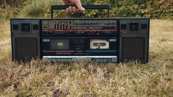 Ada tape recorder retro tua di rumput. Wanita mengambil perangkat dengan menangani — Stok Foto