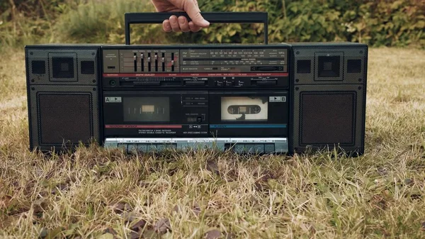 Na trawie jest stary magnetofon retro. Kobieta chwyta urządzenie za uchwyt Obraz Stockowy
