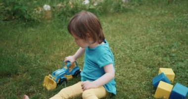 Küçük, sevimli çocuk çimlerin üzerinde arabalarla oynuyor. Çocuk kazıcıyı yere yuvarlıyor.