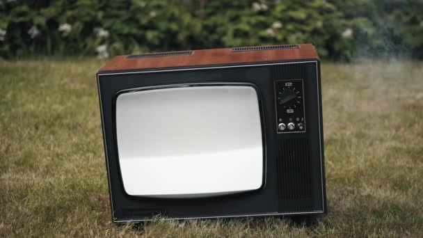 Старый старинный ретро-телевизор стоит на траве. Дымовые волны от поврежденного устройства — стоковое видео