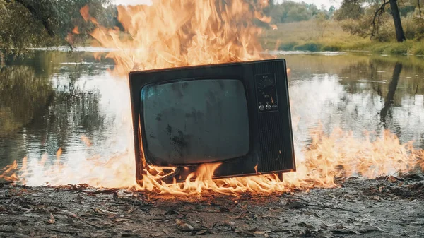 La vieja televisión vintage está ardiendo con fuego cerca del agua. El agua también está ardiendo. —  Fotos de Stock