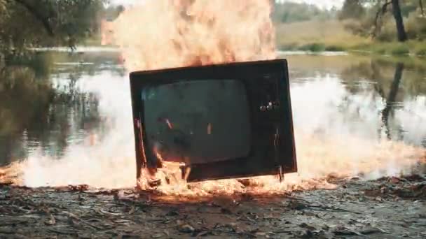 Alter Retro-Fernseher flammt auf und brennt neben dem Fluss — Stockvideo