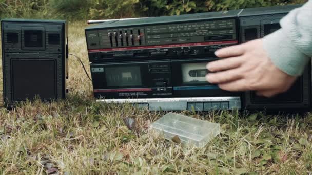 Há um gravador de fita retro na grama. Homem insere cassete de filme no dispositivo — Vídeo de Stock