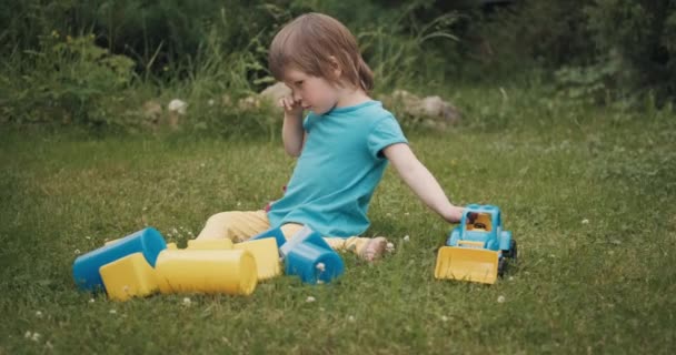 Pequeño niño caucásico está sentado en la hierba y llorando en voz alta — Vídeos de Stock