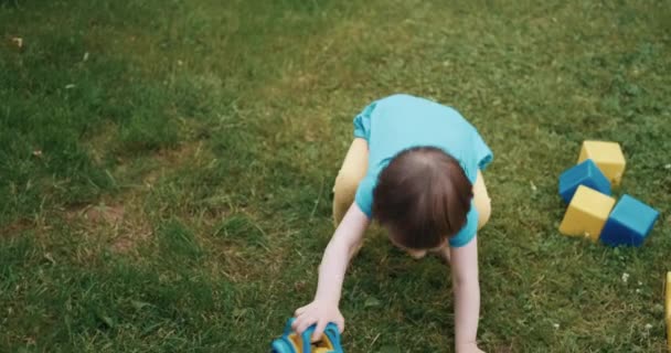 Enfant joue avec les voitures et les cubes sur l'herbe verte. Niveleuse à rouleaux pour enfants au sol — Video