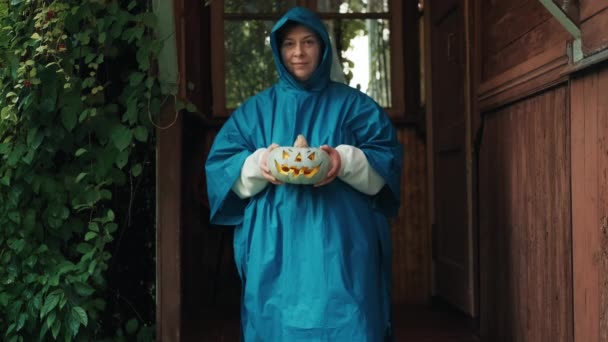 Mujer en un impermeable con una calabaza para Halloween en el porche de una casa vieja — Vídeos de Stock
