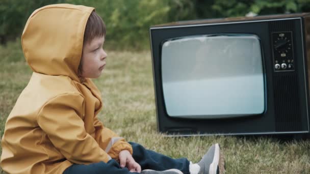 Malé, roztomilé dítě oblečené ve žluté pláštěnce s kapucí se dívá na staré, retro TV — Stock video