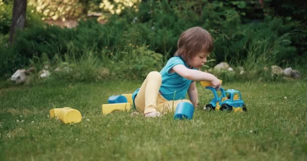 Ett litet barn leker på gräs med leksaksbilen. Sen tar han leksaken och går. — Stockvideo