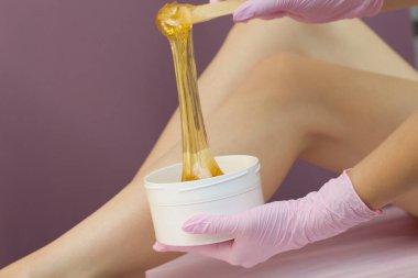 Lüks bir spa stüdyosunda saç kesimi. Kadınların ayakları sakarinle ağda yapar. Sıcak şeker. Balmumu kasesinin ürünü. Salon bankasında. Mor, eflatun arkaplan