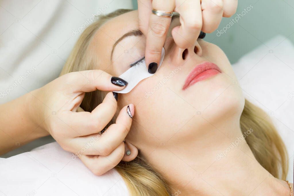 A young woman is glued a patch under her eyes, before the procedure of eyelash extension. Artificial extended eyelashes