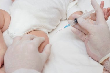 Doktorun elleri lastik koruyucu eldivenlerle şırınga tutuyor. Aşıyı bacaktan alan bir bebek. Hastanedeki çocuk doktorunu ziyaret et. - İki aylık bir bebek. Kapatmak için.