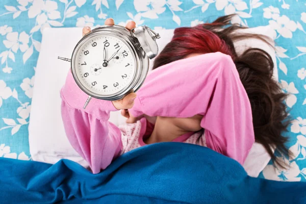 Menina na cama cobrindo os olhos e segurando despertador — Fotografia de Stock