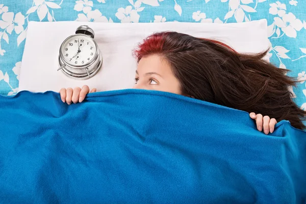 Menina escondida sob um cobertor olhando para o despertador — Fotografia de Stock