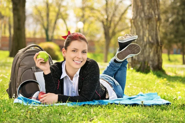 Jovem deitada em um prado segurando uma maçã — Fotografia de Stock