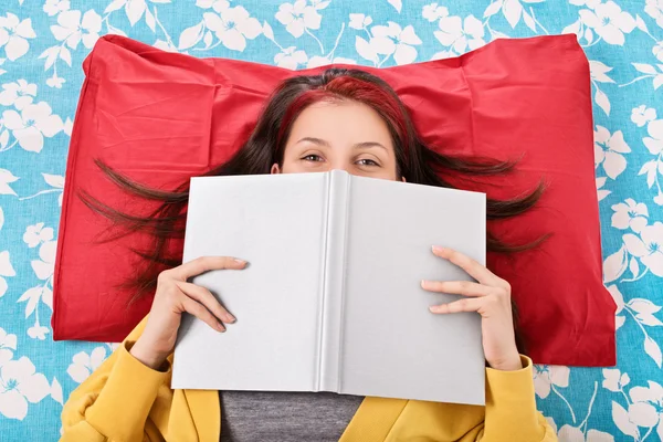 Flicka i sängen döljer ansiktet bakom en bok — Stockfoto