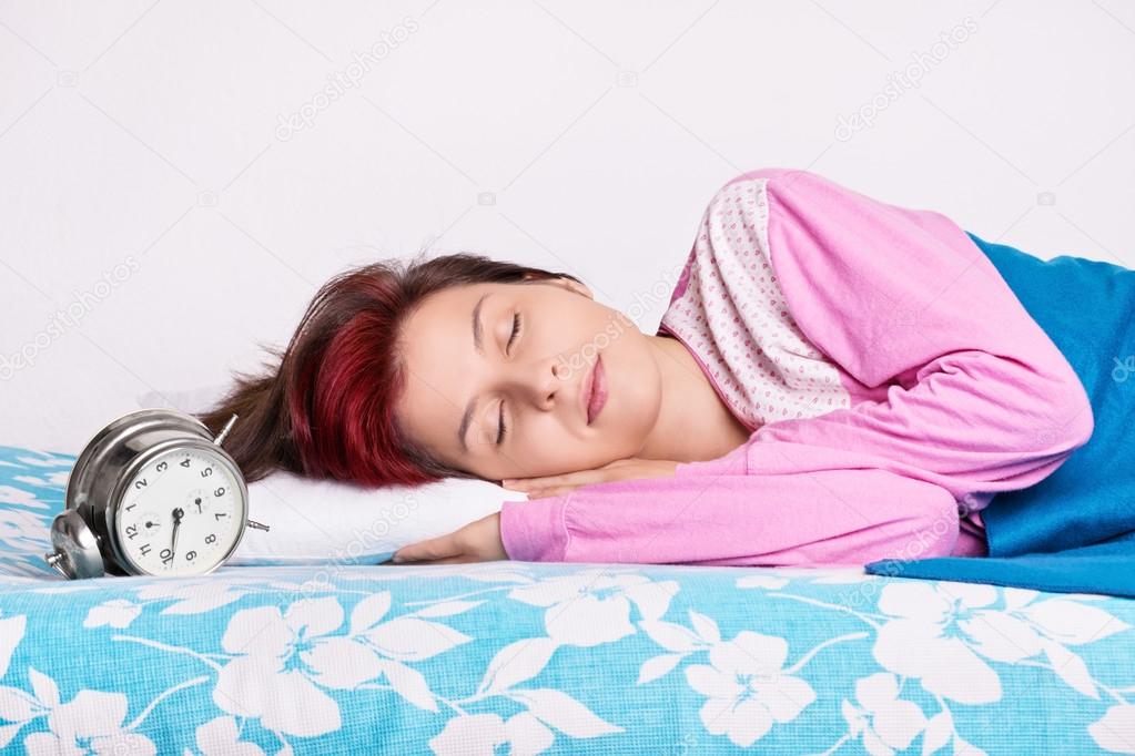 Girl in her bed sleeping next to the alarm clock