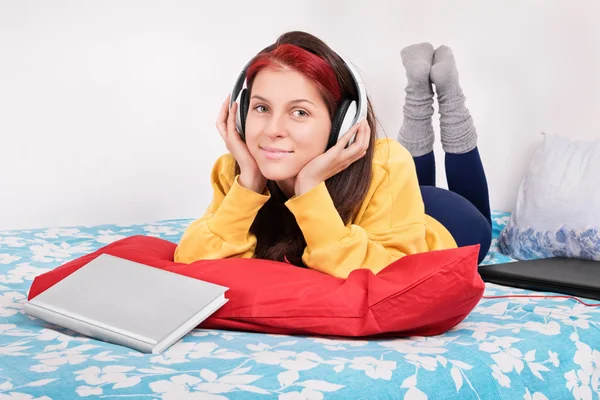 Girl in bed with headphones, book and a laptop — Stock Photo, Image