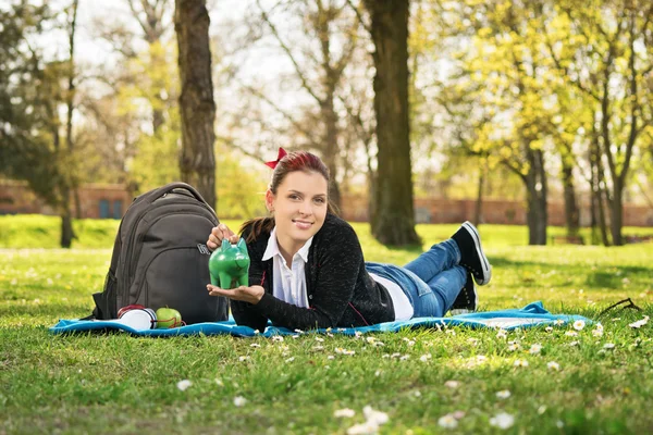 Estudiante acostado en un prado sosteniendo una alcancía — Foto de Stock