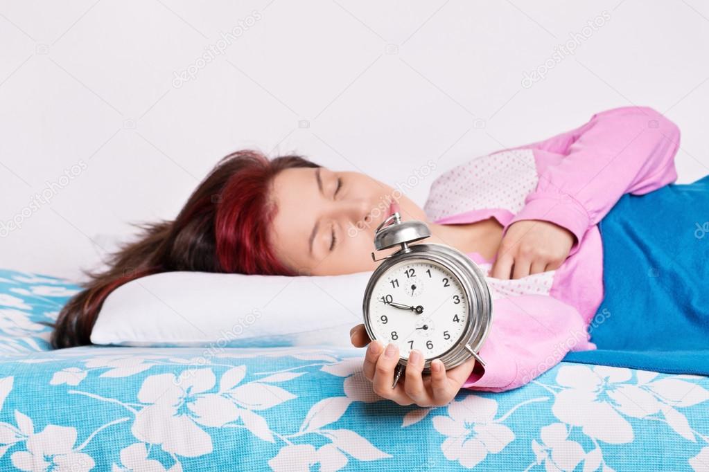 Young woman fallen asleep with alarm clock in hand