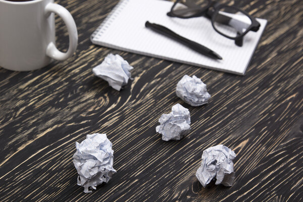Crumpled paper balls with eye glasses mug, pen and notebook