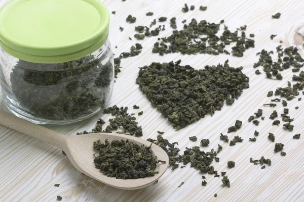 Hoja de té verde en forma de corazón, cuchara sobre fondo de madera — Foto de Stock